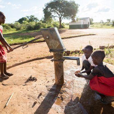 Two girls and a boy collect water from a hand pump