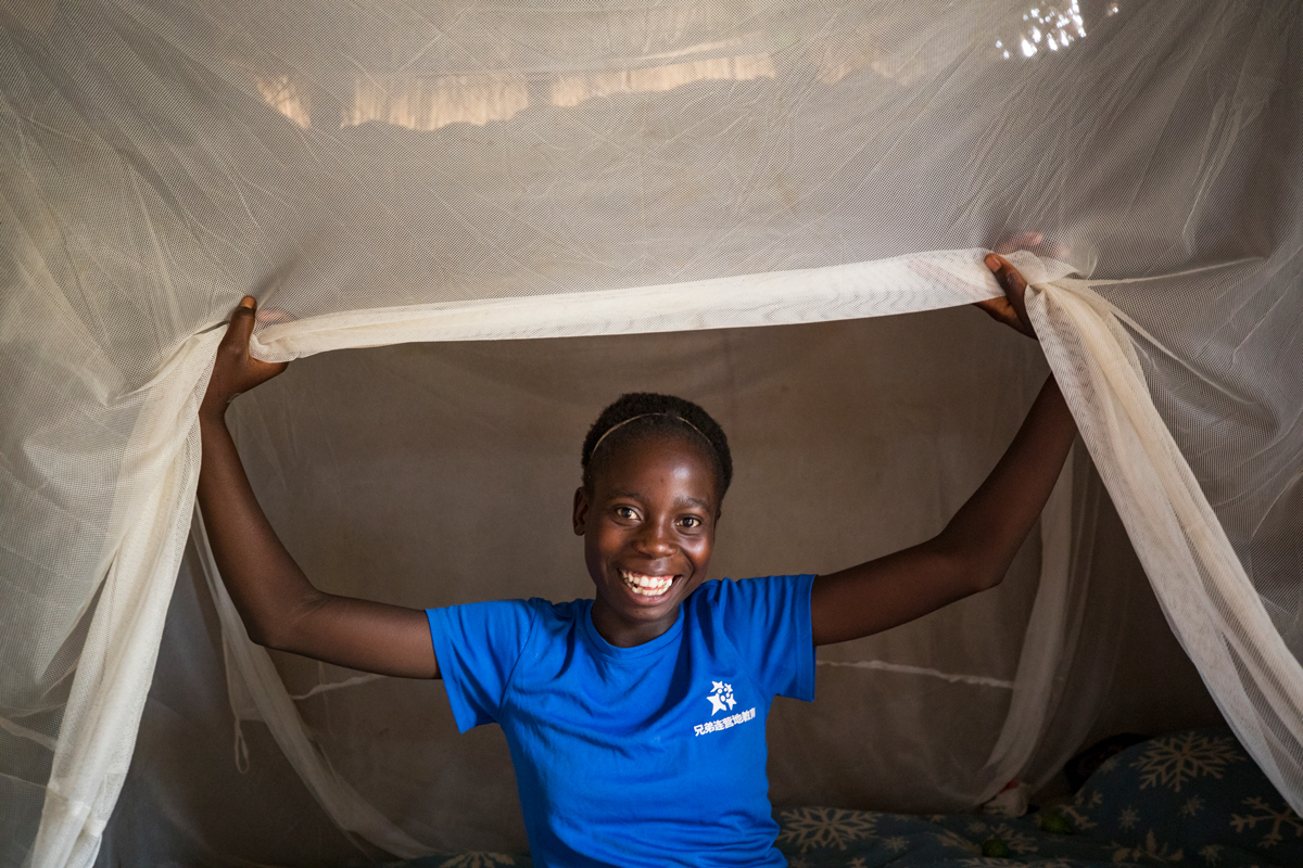 A happy young girl under a mosquito net in her room in Zambia.
