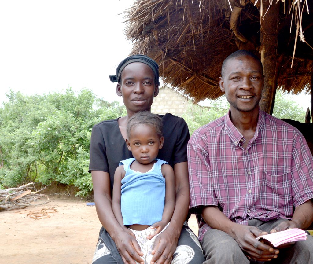A two-year-old girl with her mother and father outside their home in Zambia